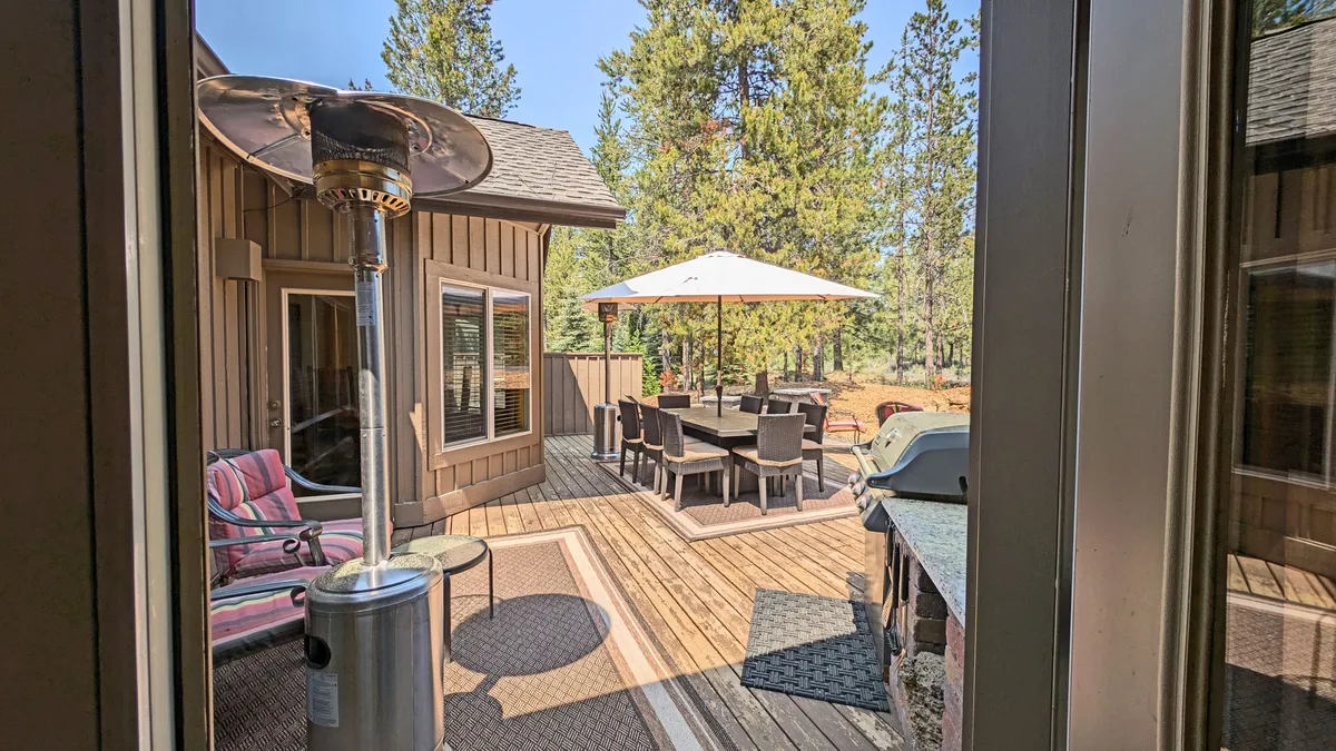 An expansive outdoor dining area featuring a table with umbrella, multiple seating options, a grill, and a patio heater. The landscaping and open-air setup make it ideal for group meals, celebrations, or after-dark gatherings.