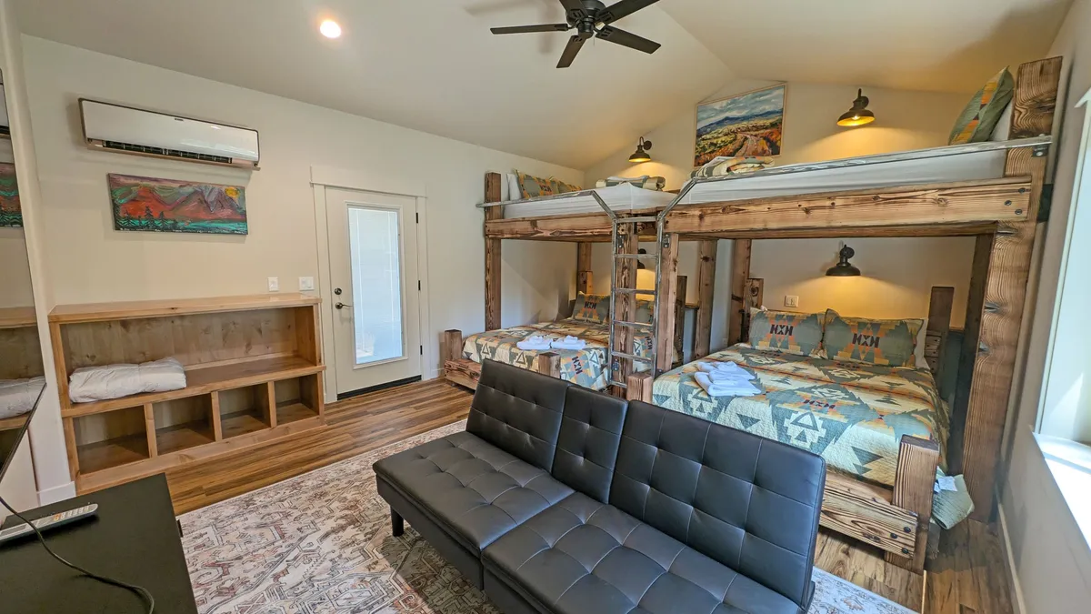 A playful, comfortable room with bunk beds, a sofa, eye-catching wall art, and a wooden bench. The space is arranged to encourage social interaction, relaxation, and group fun, reflecting the youthful and versatile nature of the area.