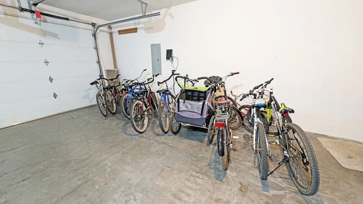 A view of the garage with several bicycles and the garage door visible, as well as a utility panel. The scene is practical, focused on bike storage and easy access for outdoor explorations.