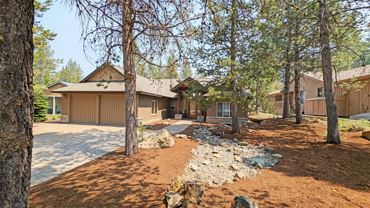 This image shows the main entrance of the house, framed by a landscaped front yard and a welcoming driveway. The setting is relaxed and inviting, with children playing in the yard and family members gathering on the porch, hinting at the playful resort lifestyle just steps away.