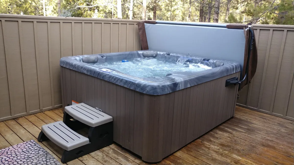 An exterior shot featuring a private hot tub on a wooden deck, with steps leading up and surrounded by serene outdoor scenery. This tranquil setting invites relaxation after active days spent exploring.