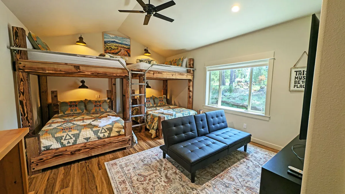 A spacious bunk room with multiple bunk beds, a sofa for lounging, and a window offering natural views. The setup is playful and perfect for groups or families, with space for sleeping, playing games, and sharing stories.