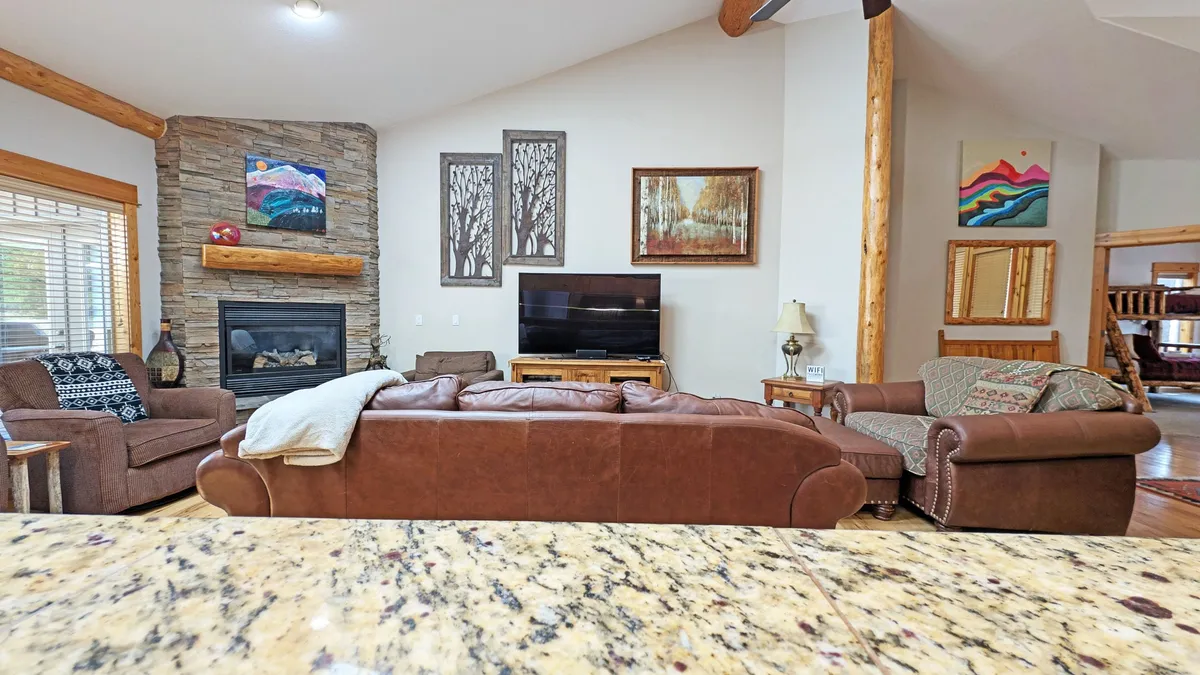 A spacious living room featuring a striking stone fireplace as a focal point. Leather sofas are arranged for comfortable seating, facing a large television mounted above the fireplace. The room is accessorized with tasteful artwork and warm ambient lighting, creating a cozy and inviting atmosphere ideal for gatherings and relaxation.