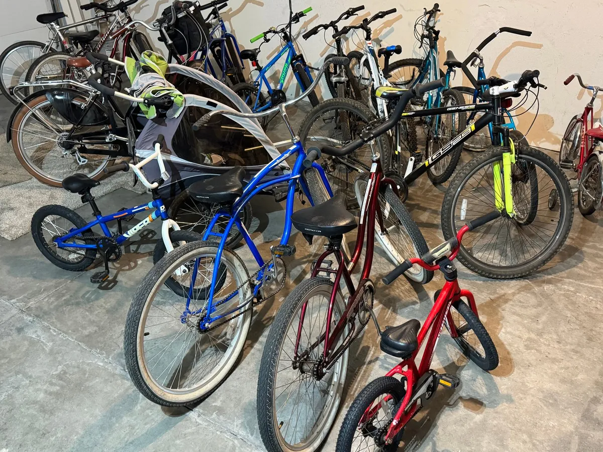 The image displays a vibrant assortment of bicycles ready for family outings, with colorful frames and accessories lined up in a playful, energetic setting. It evokes active family adventures and the joy of exploring Sunriver’s trails and amenities.