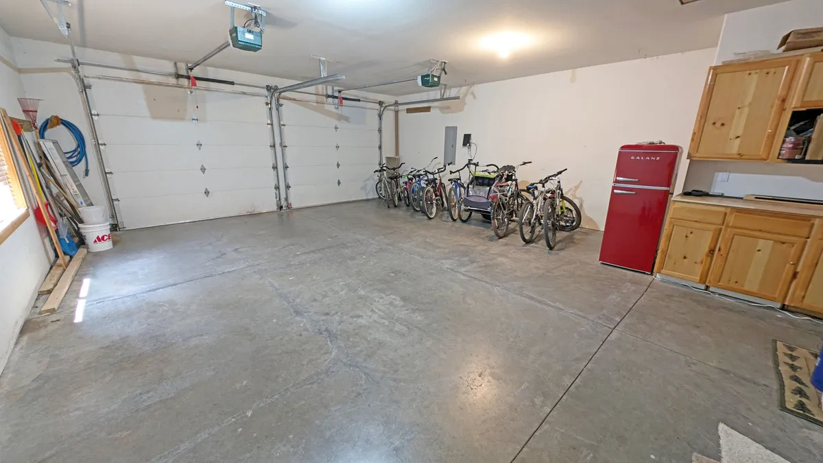 This image showcases a section of the garage containing multiple bicycles, a red refrigerator, and wooden cabinets. The arrangement is practical and inviting, emphasizing ample storage and readiness for adventure.